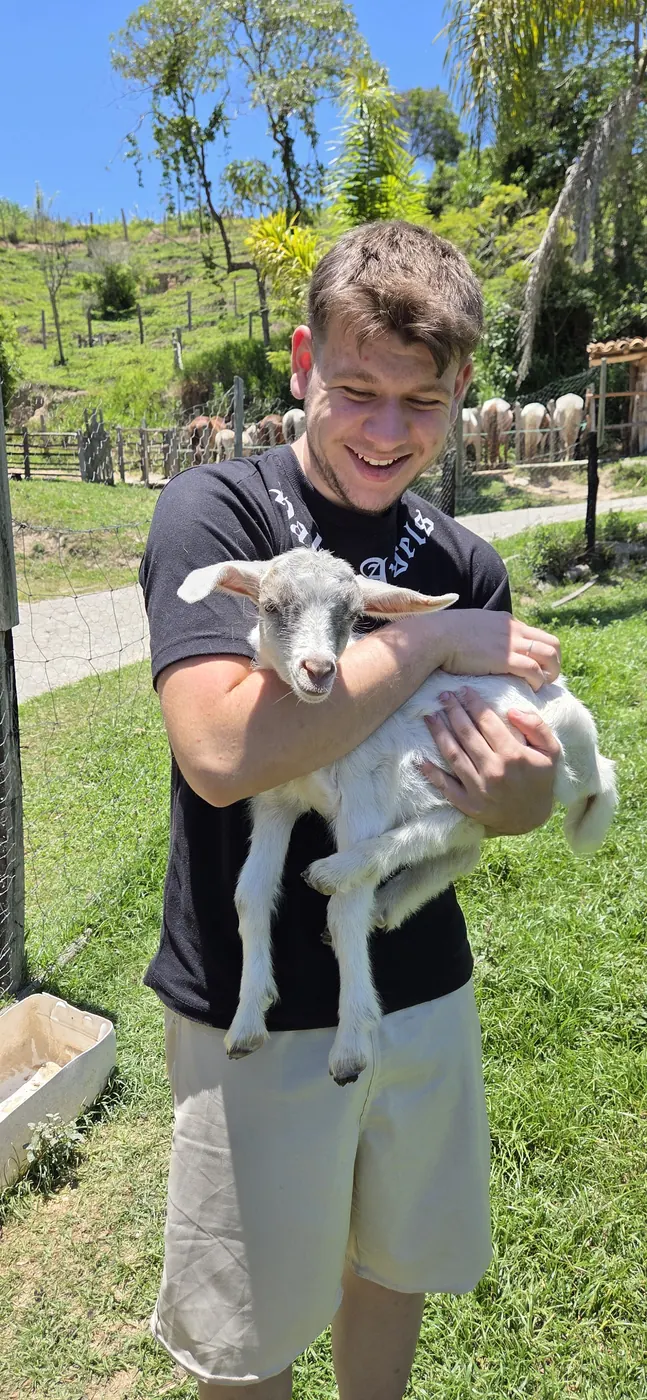 Menino segurando um cabritinho no gramado da fazenda