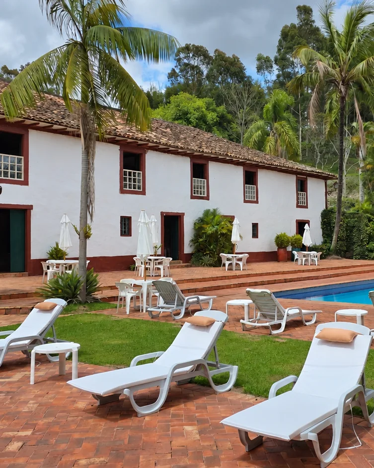Casarão do Hotel Fazendão ao lado da piscina, com espreguiçadeiras no deck de tijolo