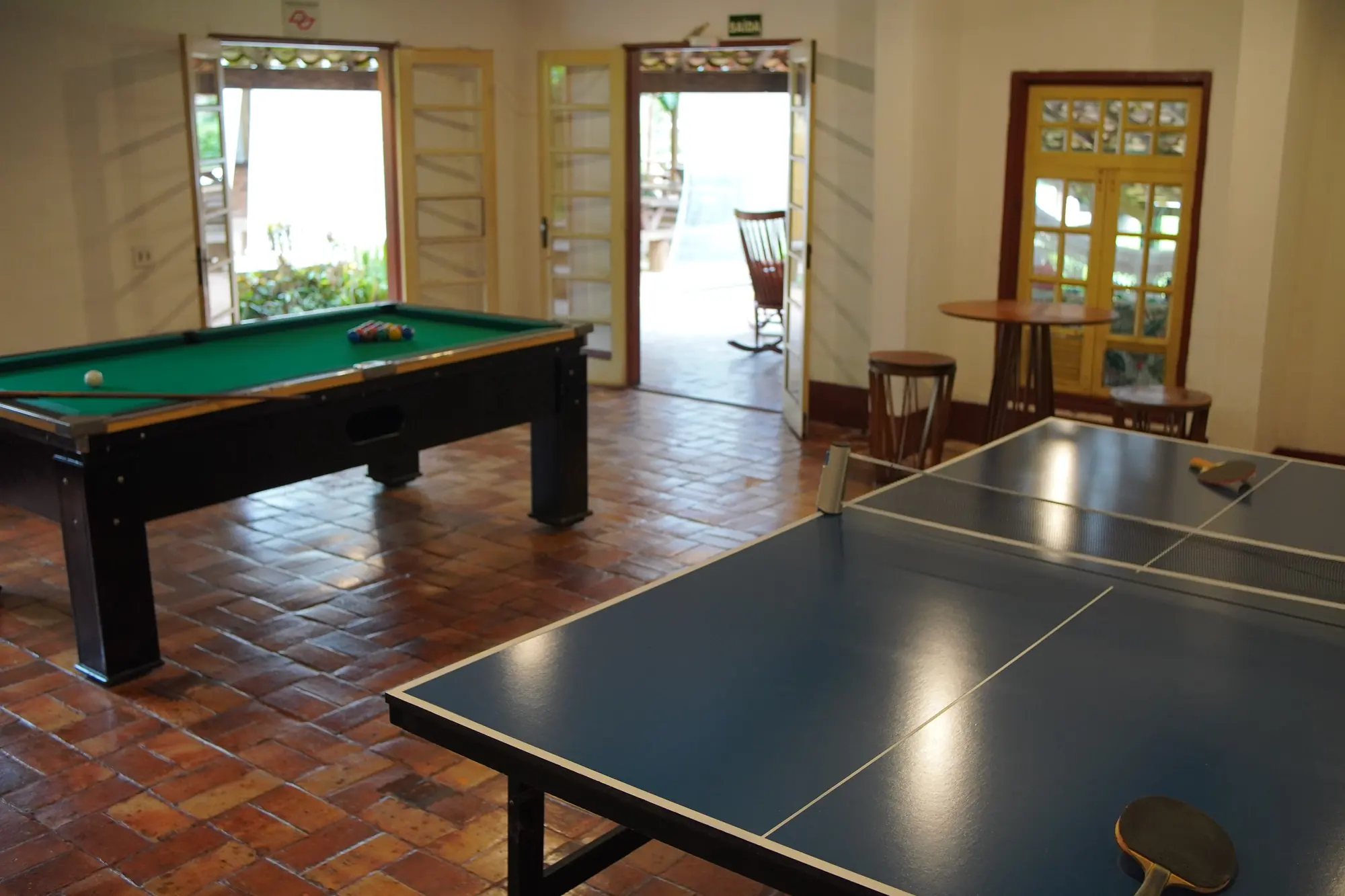 Salão de jogos com mesa de pingue-pongue, sinuca e portas abertas para a varanda