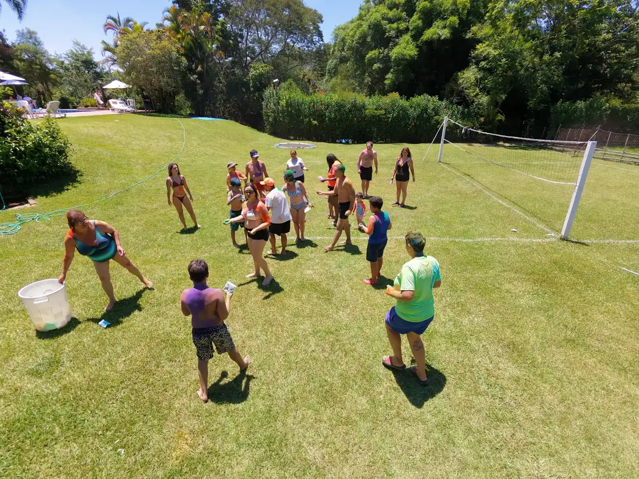 Famílias em brincadeira de recreação no campo de vôlei gramado, com a piscina ao fundo