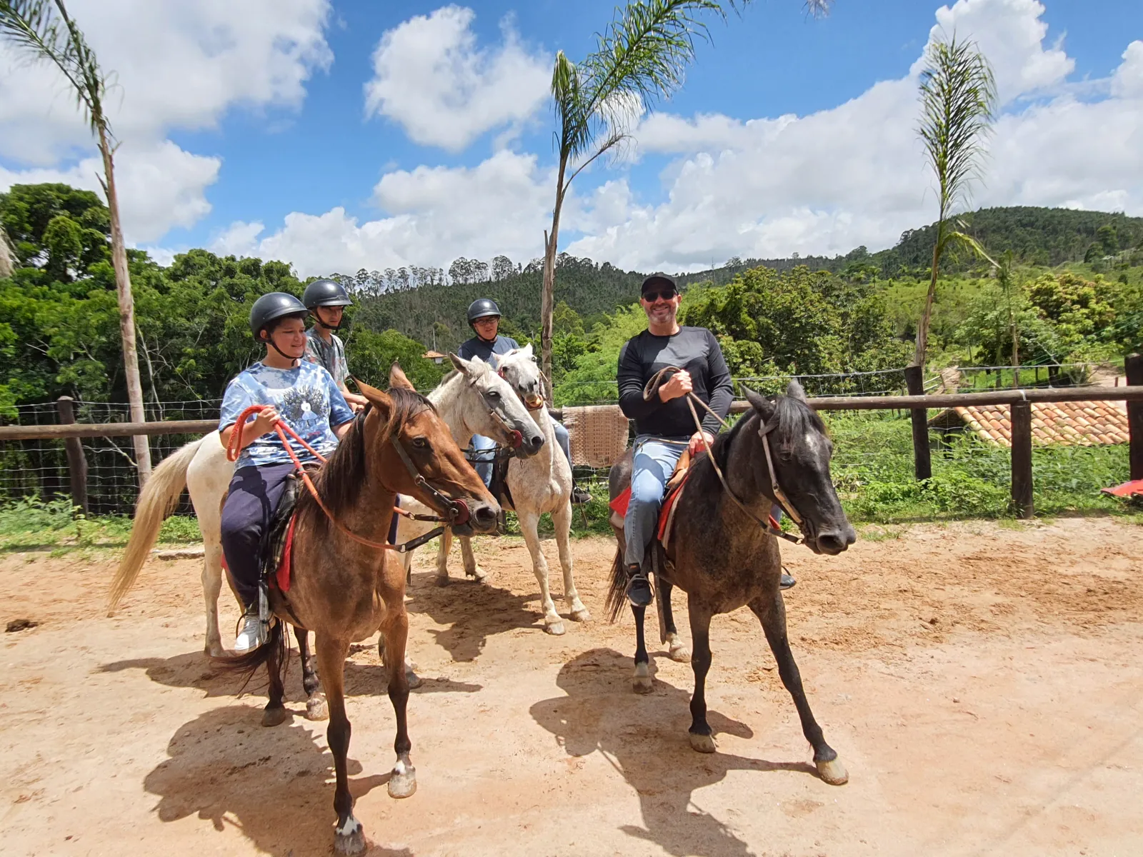 Grupo a cavalo, de capacete, no picadeiro do Hotel Fazendão entre as palmeiras